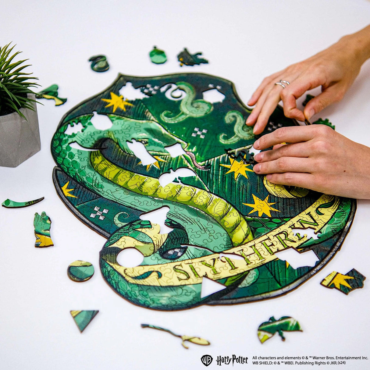 Hände setzen ein Slytherin-Wappen-Puzzle mit einer Schlange und Sternen zusammen