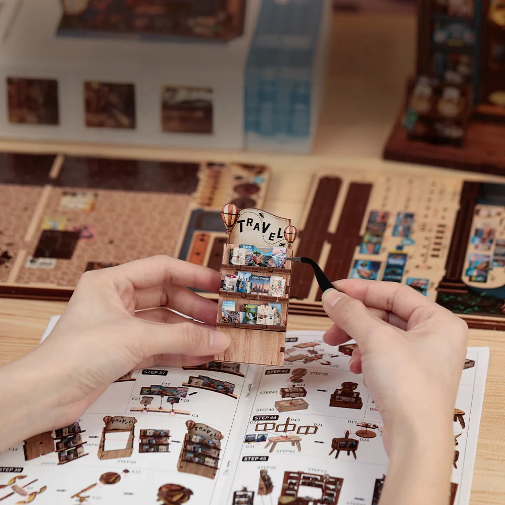 Hände bauen ein Miniatur-Reise-Bücherregal mit Pinzette und Anleitung