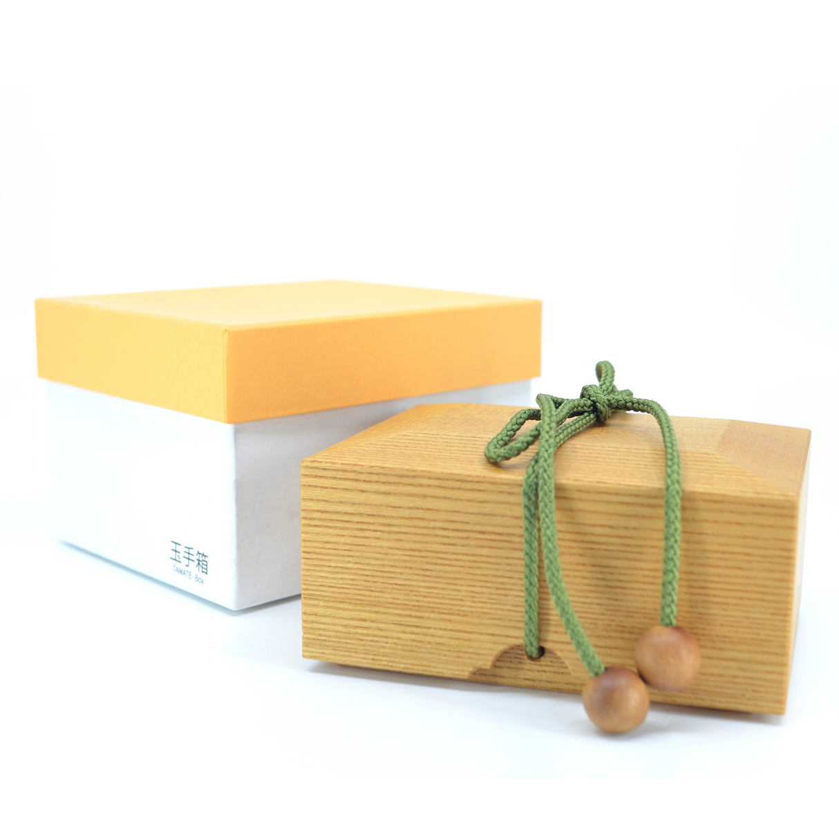 Holzschatulle mit grüner Kordel und Verschlusskugeln neben einer weiß gelben Geschenkbox