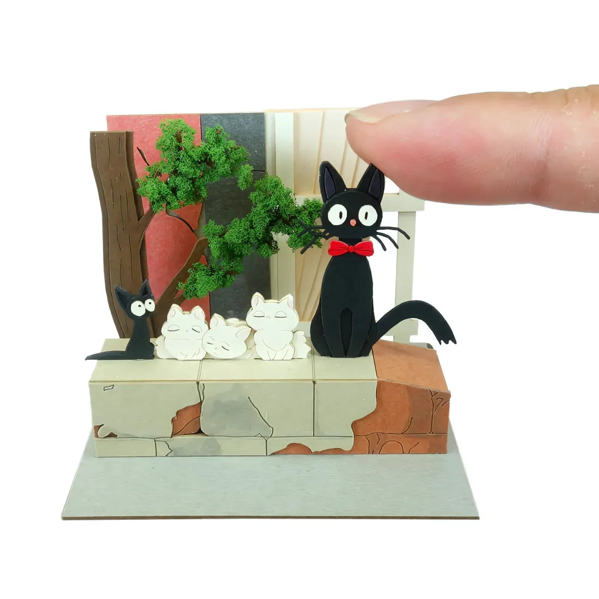 Eine Miniatur-Diorama-Szene mit einer schwarzen Katze mit roter Fliege, die auf einer Mauer sitzt