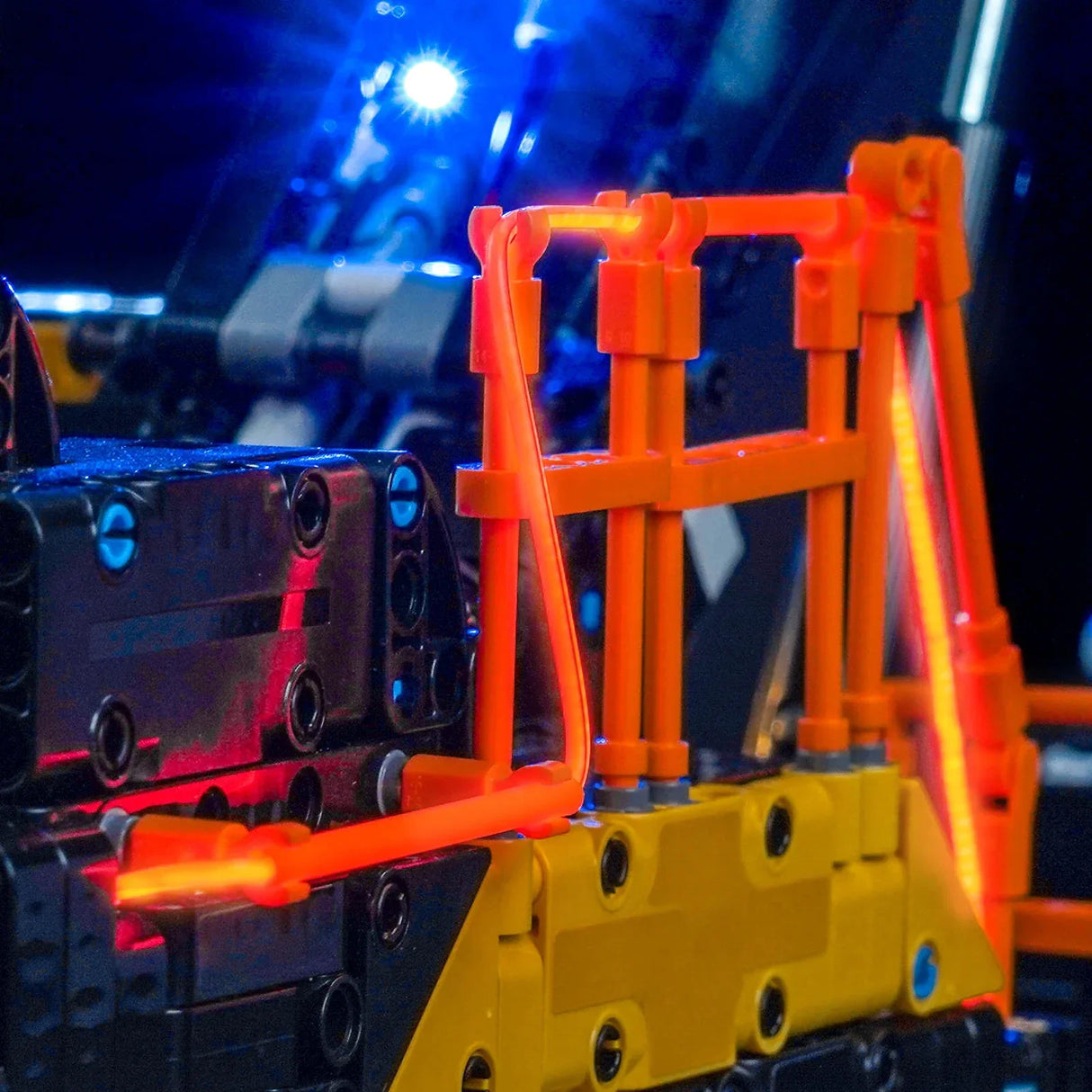 Nahaufnahme eines LEGO Technic Modells mit leuchtend orangefarbenen und gelben Teilen, blauen Lichtern im Hintergrund