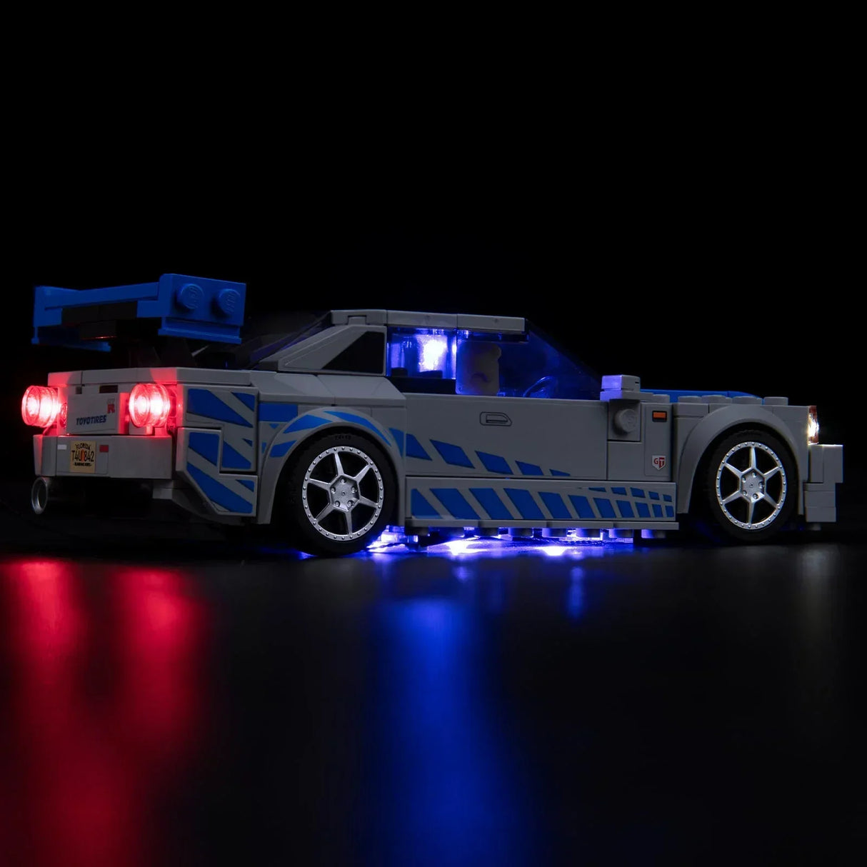 Beleuchtetes Lego Modell eines grauen Sportwagens mit blauen Streifen vor schwarzem Hintergrund