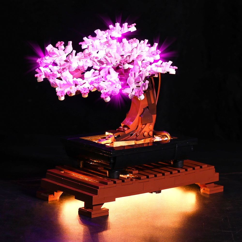 Seitenansicht des LEGO Bonsai Baums 10281 mit leuchtend rosa LED-Lichtern in den Kirschblütenkronen und warmem Lichtschein unter dem hölzernen Sockel.