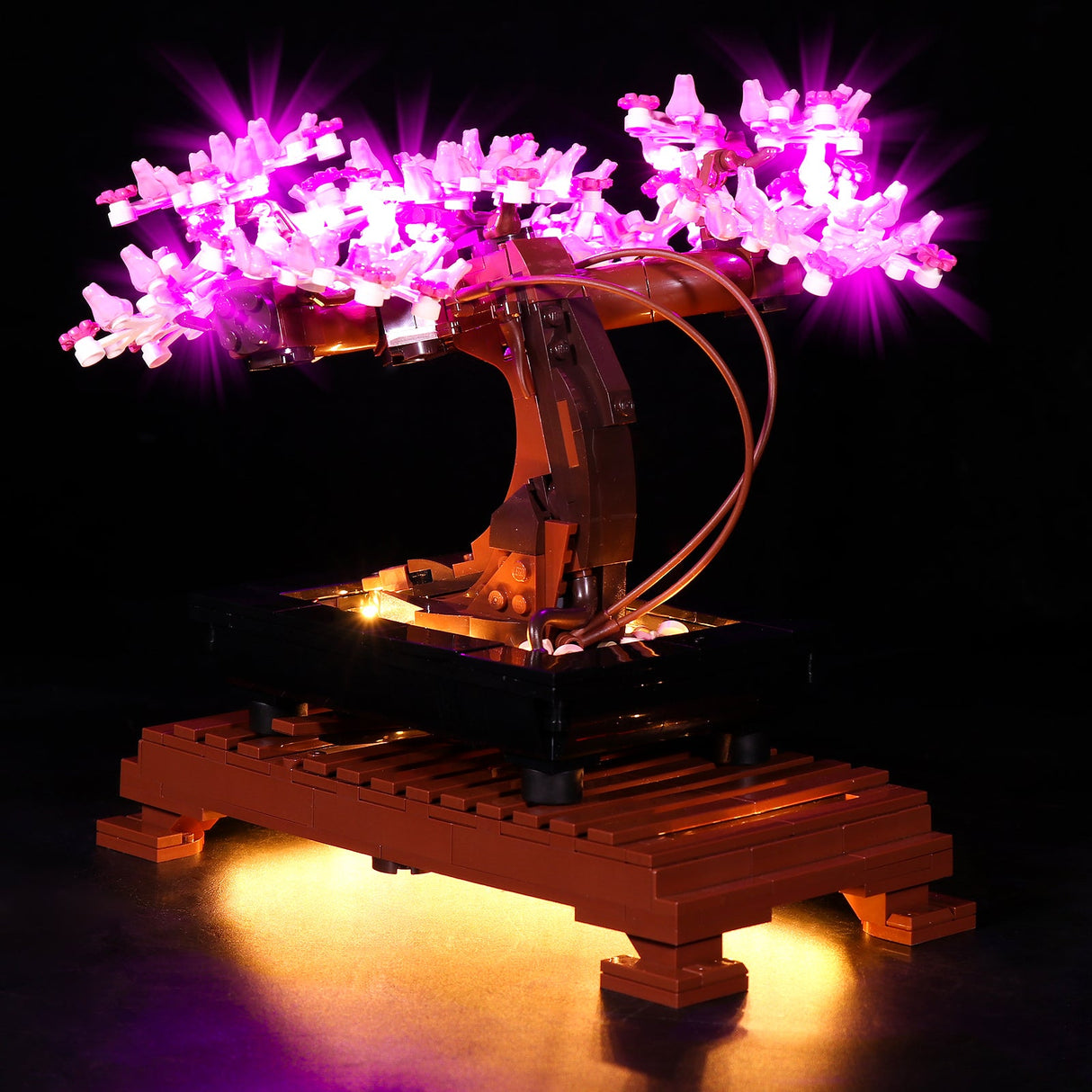 Rückansicht des LEGO Bonsai Baums mit sichtbaren, dezent verlegten Kabeln des LED-Beleuchtungssets, das die rosa Blüten und die Unterseite des Modells illuminiert.