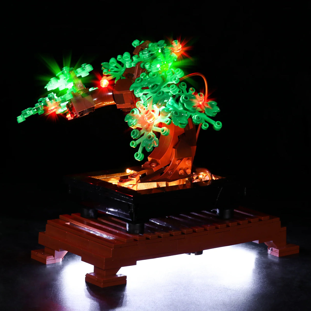 Eine leicht von unten fotografierte Ansicht des LEGO Bonsai-Baums. Die Kameraperspektive betont die Unterseite der Blätter und die Struktur des Stammes. Die warmweißen LEDs in der Schale leuchten die Unterseite des grünen Blätterdachs golden aus, ergänzt durch die strahlenden roten und grünen Lichtpunkte.