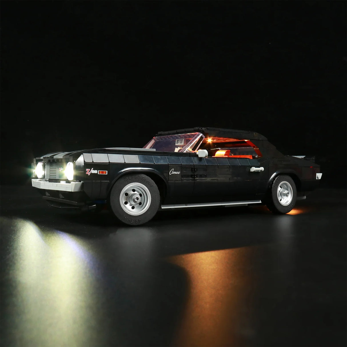 LEGO Chevrolet Camaro Z28 (Set 10304) als Modellauto in Schwarz mit eingebautem LED-Beleuchtungsset. Seitenansicht von vorne mit leuchtenden Scheinwerfern und rot illuminiertem Innenraum auf dunklem Hintergrund.