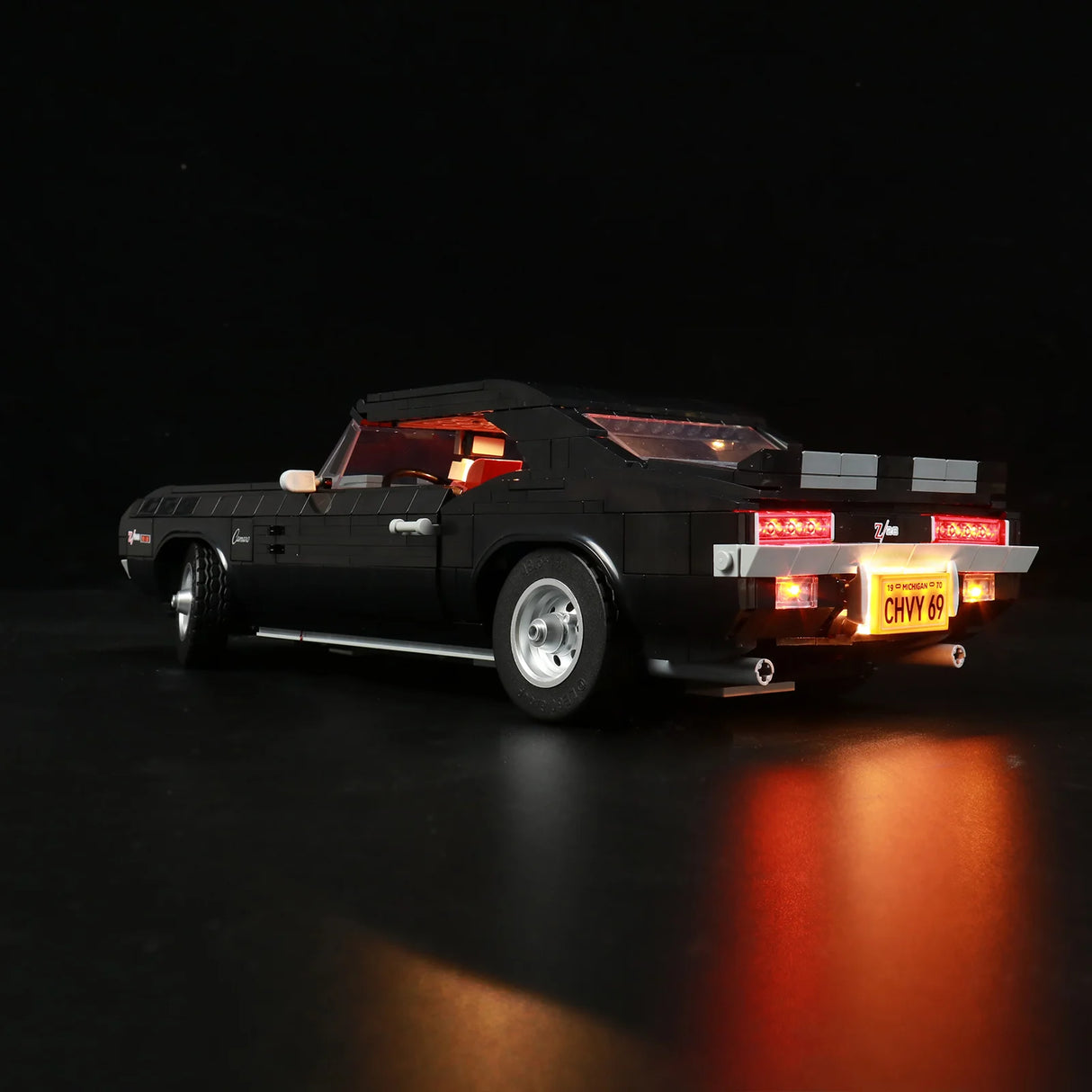 Heckansicht des LEGO Chevrolet Camaro Z28 (10304) mit aktivem LED-Lichtset. Zu sehen sind die leuchtenden roten Heckleuchten, das beleuchtete „CHVY 69“-Nummernschild und der rote Innenraum.