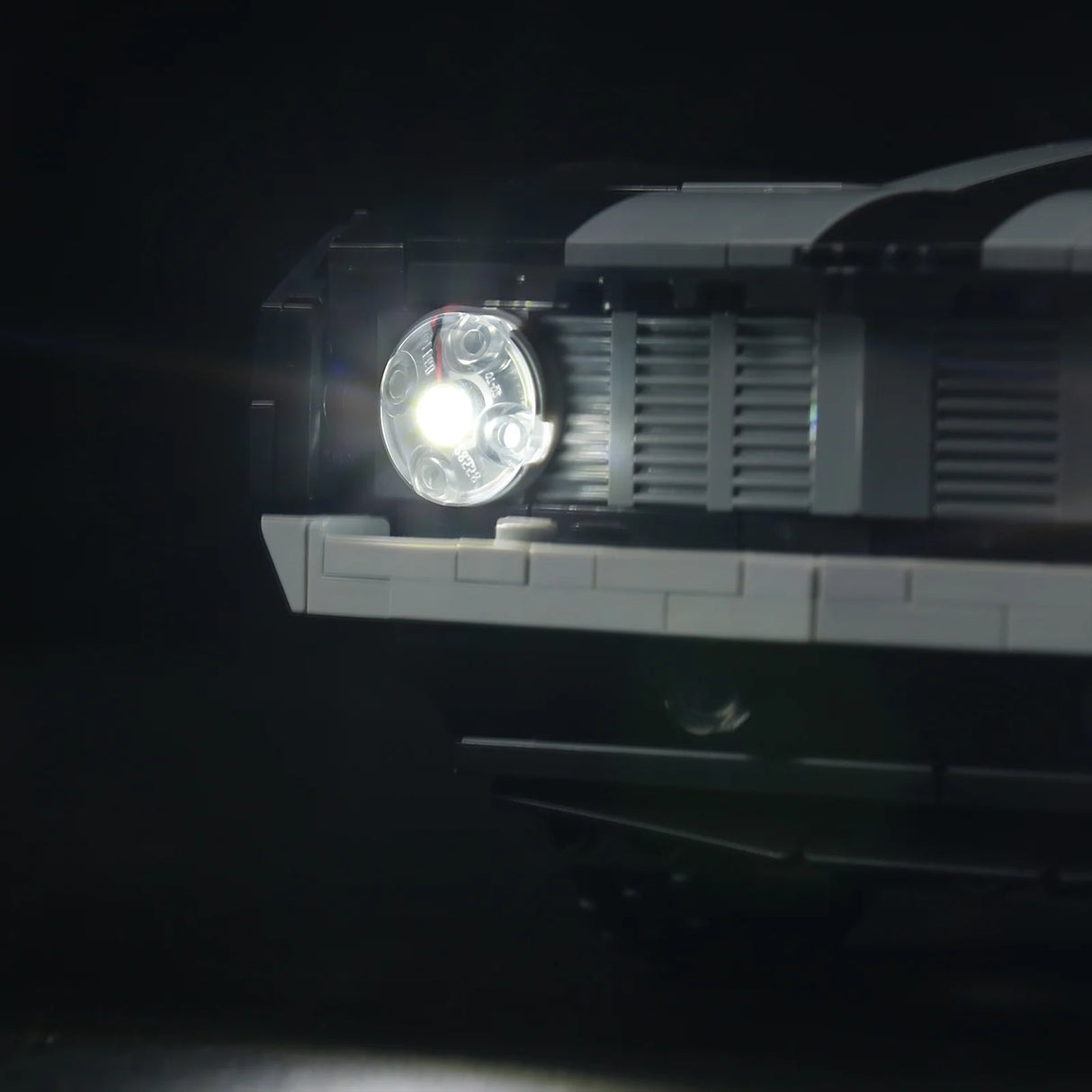 Detailaufnahme des vorderen LED-Scheinwerfers am LEGO Chevrolet Camaro Z28. Das kaltweiße LED-Licht strahlt hell durch den transparenten runden LEGO-Stein neben dem Kühlergrill.