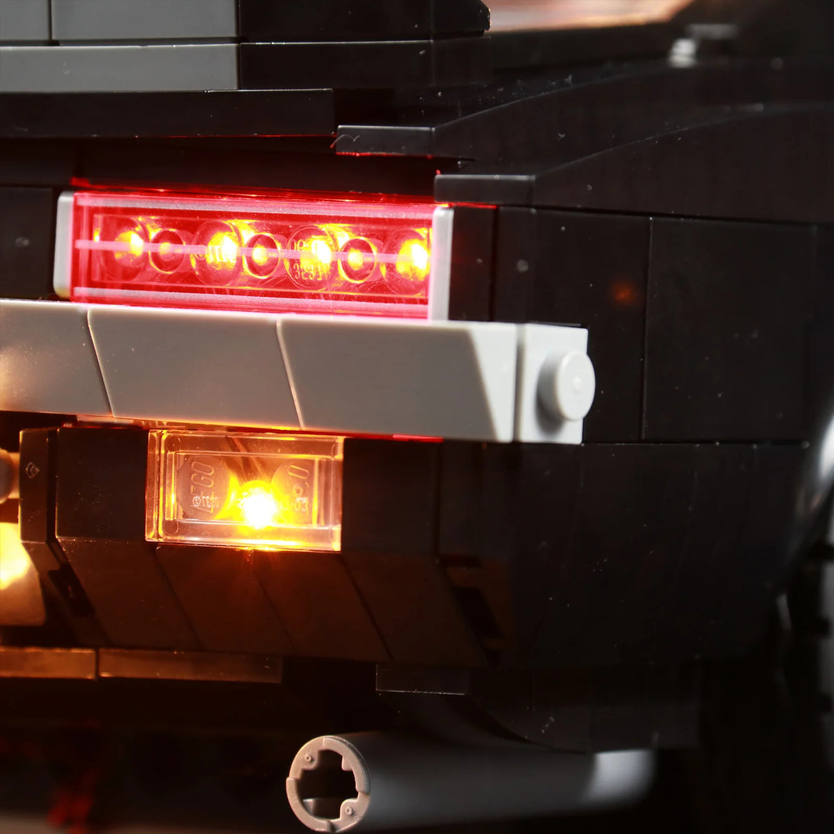 Detailansicht der Heckbeleuchtung des LEGO Chevrolet Camaro Z28. Die roten LED-Rückleuchten und die gelbe Kennzeichenbeleuchtung sind hell erleuchtet.