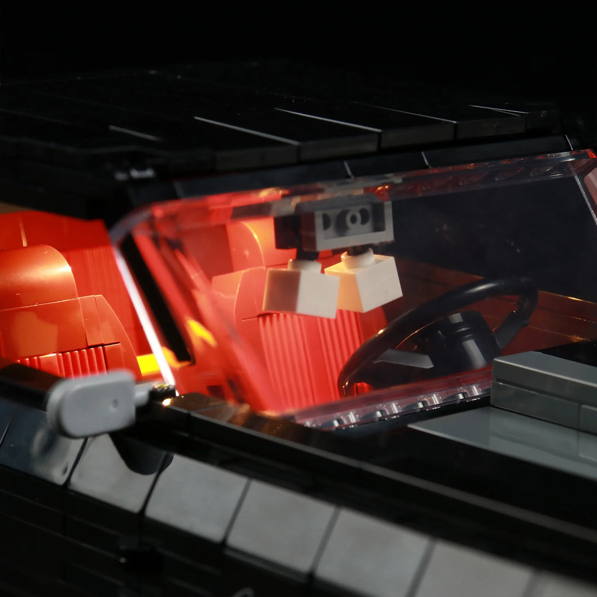 Nahaufnahme der Windschutzscheibe des LEGO Chevrolet Camaro Z28 mit LED-Innenraumbeleuchtung. Das warme rote Licht beleuchtet das Cockpit, die Sitze und das Lenkrad des LEGO-Modells.