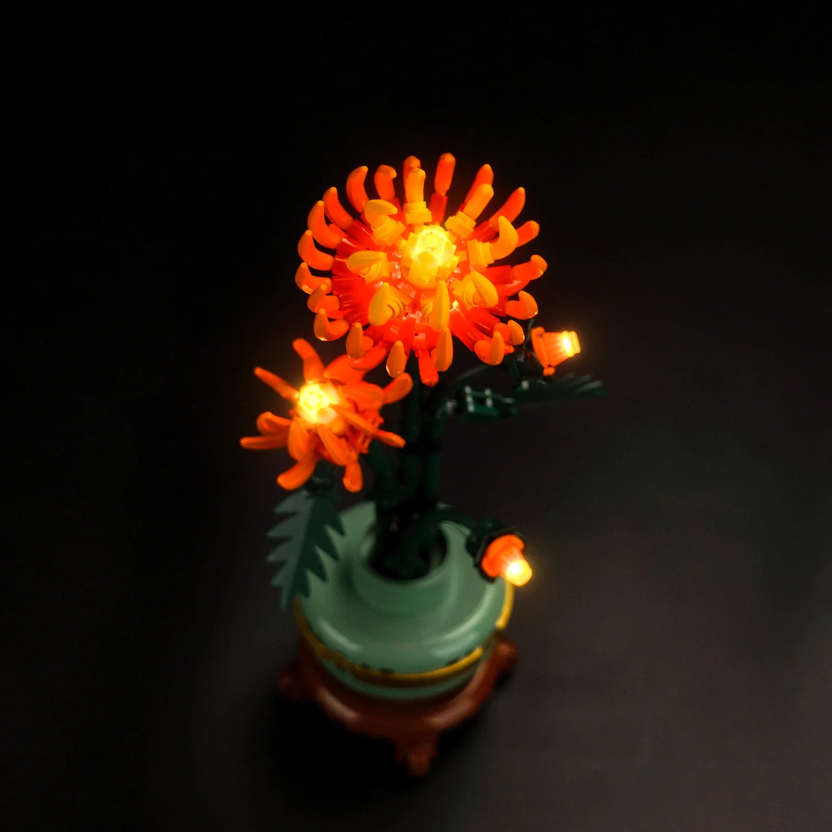 Beleuchtete orangefarbene Chrysanthemen aus Klemmbausteinen in einer Vase vor schwarzem Hintergrund