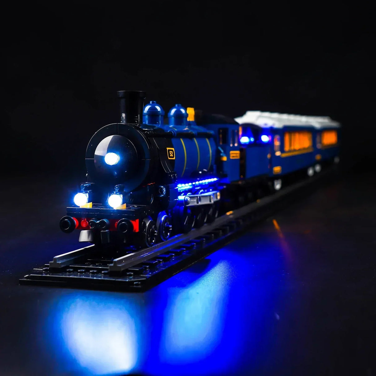 Beleuchtetes Modell einer blauen Dampflokomotive auf Schienen vor schwarzem Hintergrund