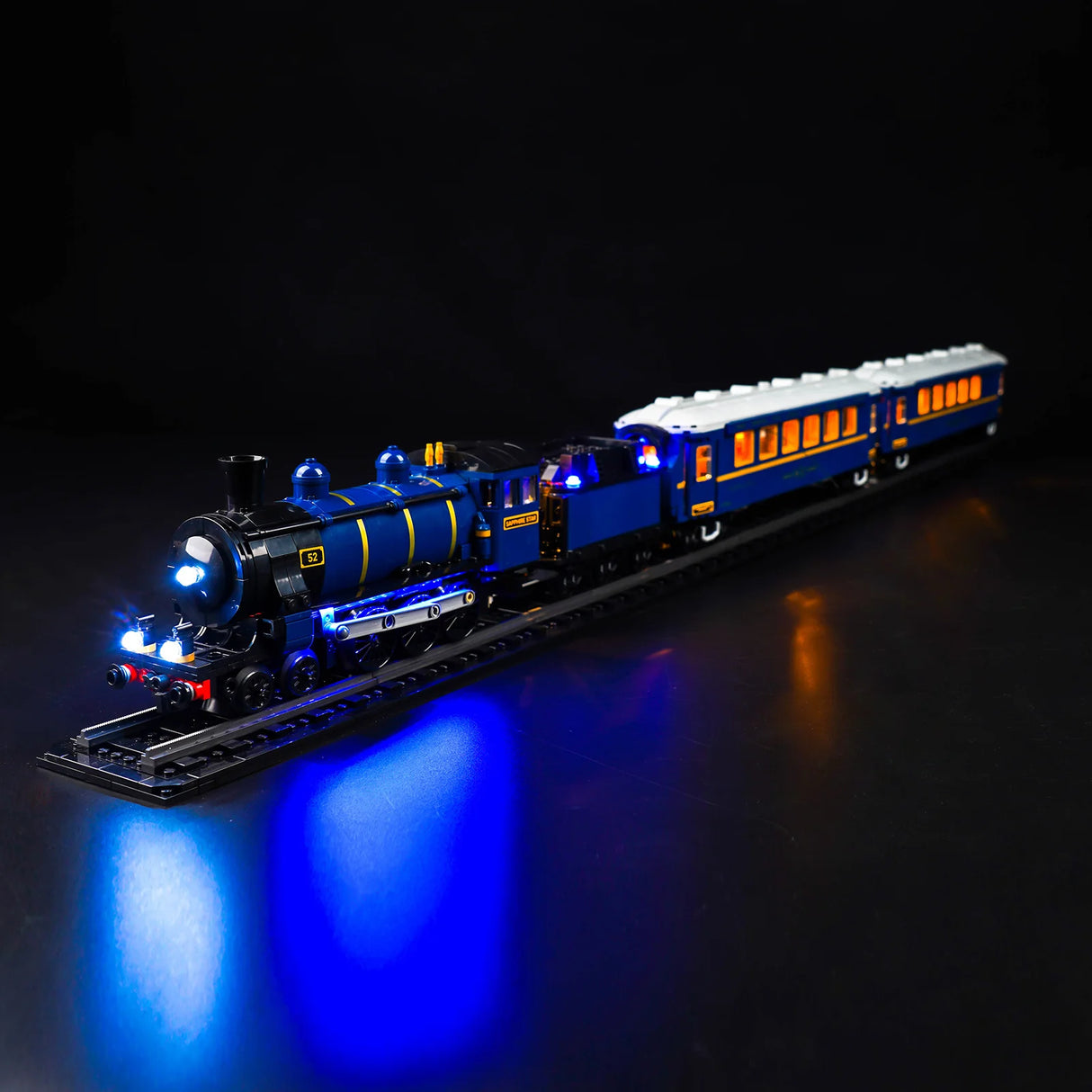 Beleuchtetes Modell einer blauen Dampflokomotive mit Personenwagen auf Schienen vor schwarzem Hintergrund