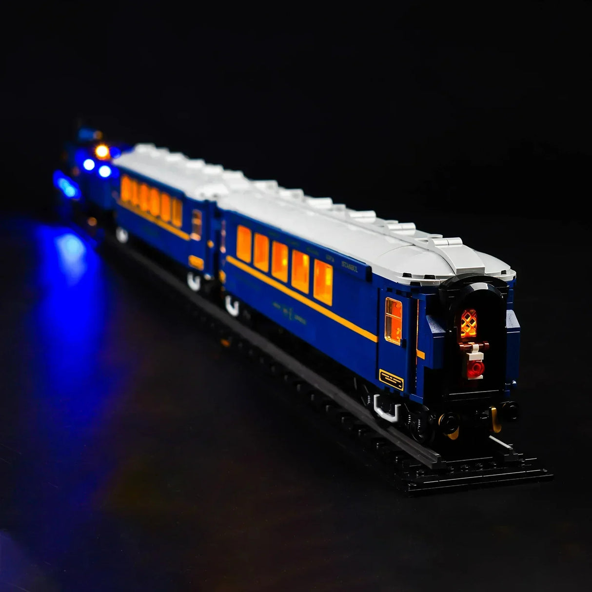 Beleuchtetes Lego Modell eines blauen Reisezugwagens auf Schienen vor schwarzem Hintergrund