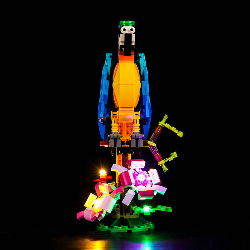 Beleuchtetes Lego Modell eines Papageis auf einem Ast vor schwarzem Hintergrund