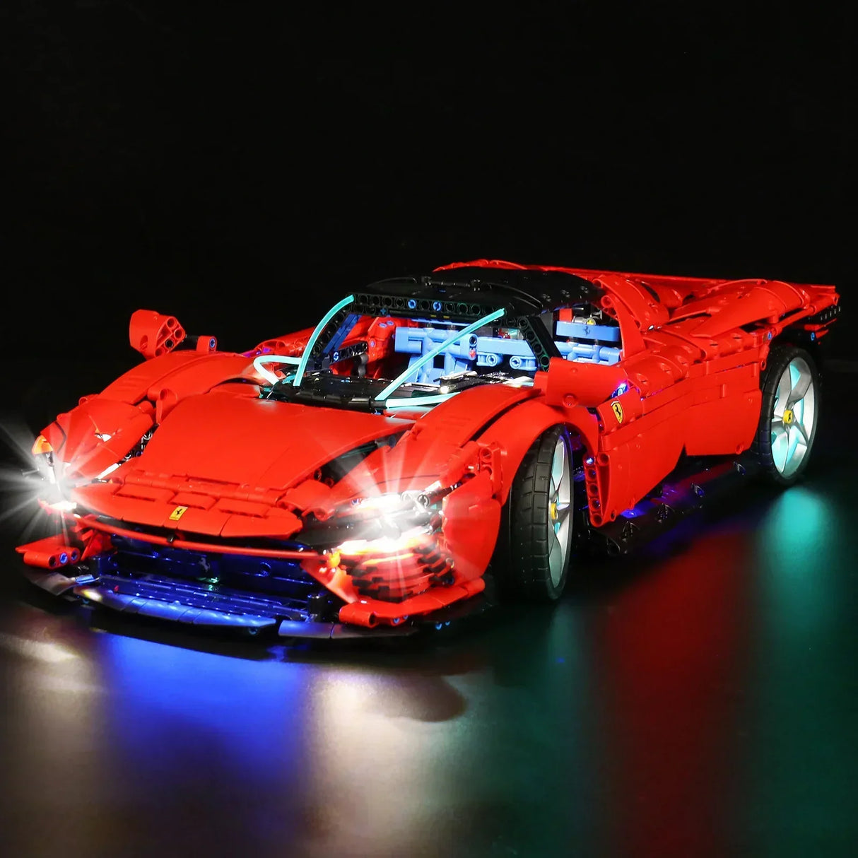 Rotes Ferrari Modellauto aus Klemmbausteinen mit eingeschalteter LED Beleuchtung vor schwarzem Hintergrund