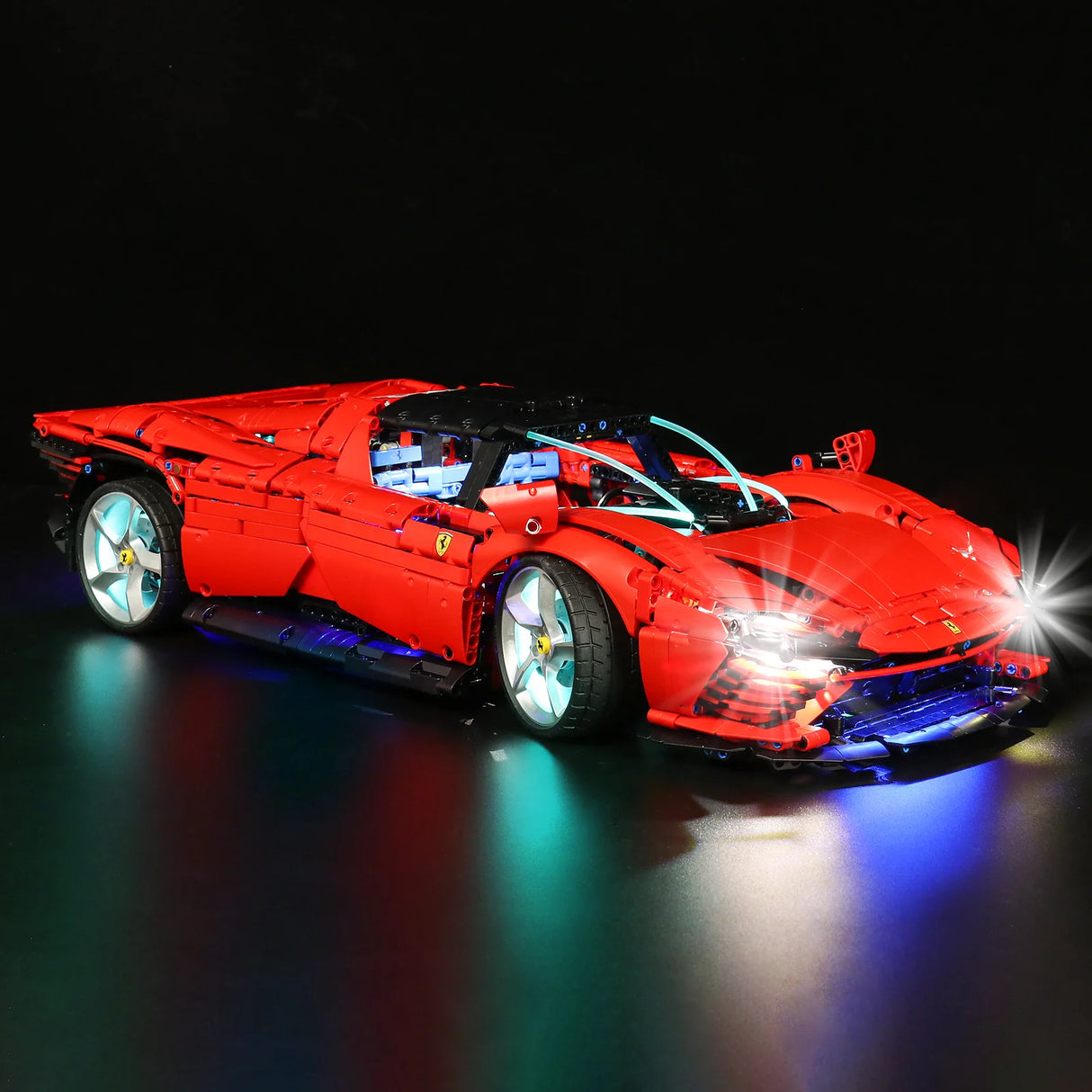 Rotes Ferrari Modellauto aus Klemmbausteinen mit eingeschalteter LED Beleuchtung vor schwarzem Hintergrund
