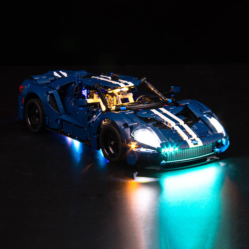 Blaues Lego Technic Modellauto mit eingeschalteter LED Beleuchtung vor schwarzem Hintergrund