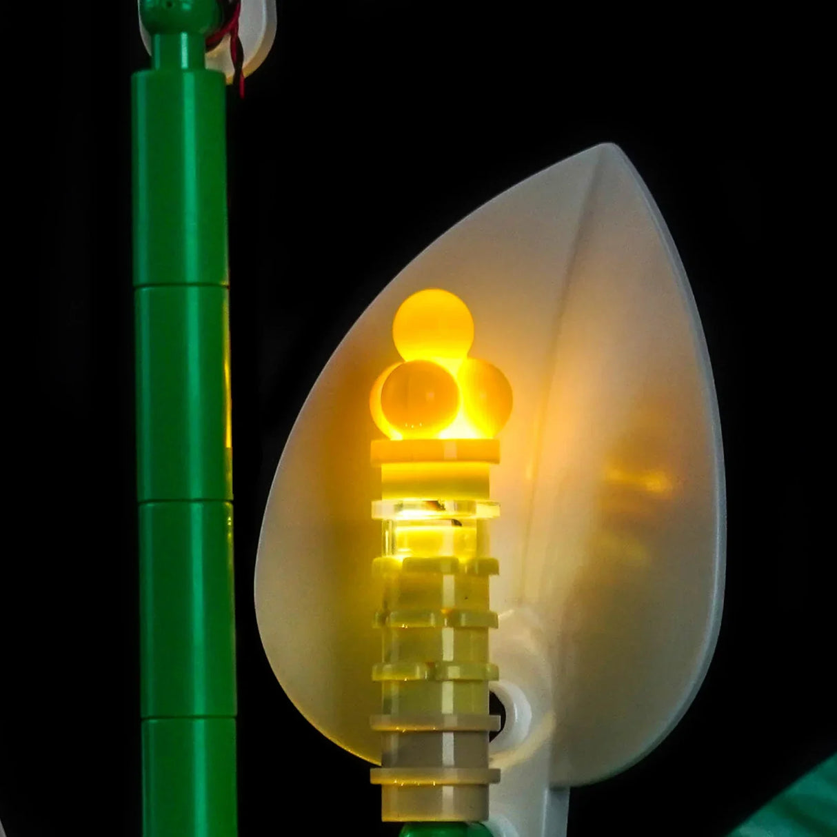 Nahaufnahme eines leuchtenden gelben Lego-Blumenstiels mit einem grünen Stiel im Hintergrund