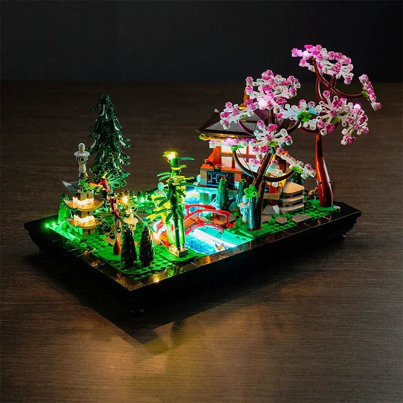LEGO Icons 10315 Garten der Stille aus seitlicher Perspektive mit LED-Beleuchtung für die grünen Bambuspflanzen, die rote Brücke und den leuchtenden Steinpavillon.