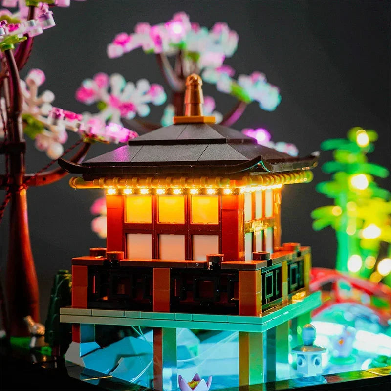 Nahaufnahme des beleuchteten LEGO 10315 Garten der Stille Pavillons mit warmweißer LED-Dachbeleuchtung und bläulich schimmerndem Wasserbecken im Hintergrund.