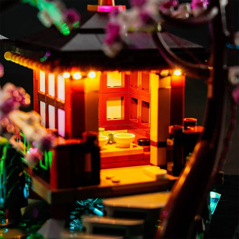 Detailansicht des LEGO 10315 Pavillon-Innenraums mit eingebauter LED-Lichtgestaltung, die das Miniatur-Teeservice in ein gemütliches, warmes Licht taucht.