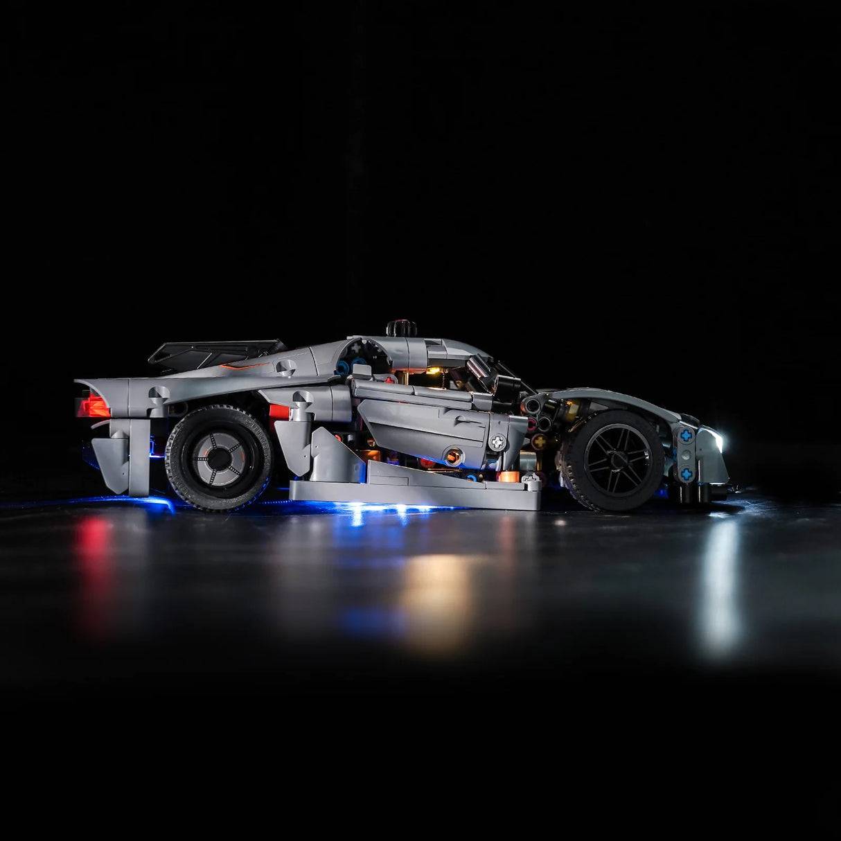 Graues Lego Technic Modell eines Sportwagens mit eingeschalteter LED Beleuchtung vor schwarzem Hintergrund