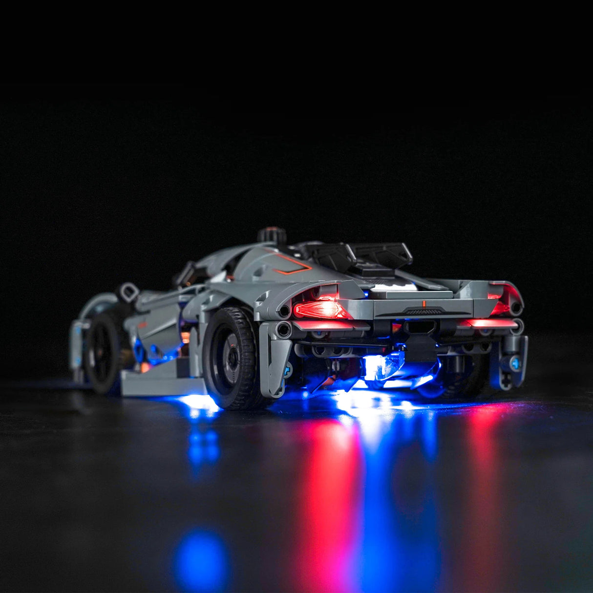 Graues Modellauto aus Klemmbausteinen mit leuchtenden roten und blauen LED Lichtern vor schwarzem Hintergrund