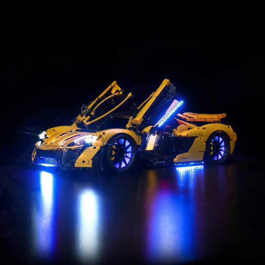 Gelbes Modellauto aus Klemmbausteinen mit blauer LED Beleuchtung vor schwarzem Hintergrund