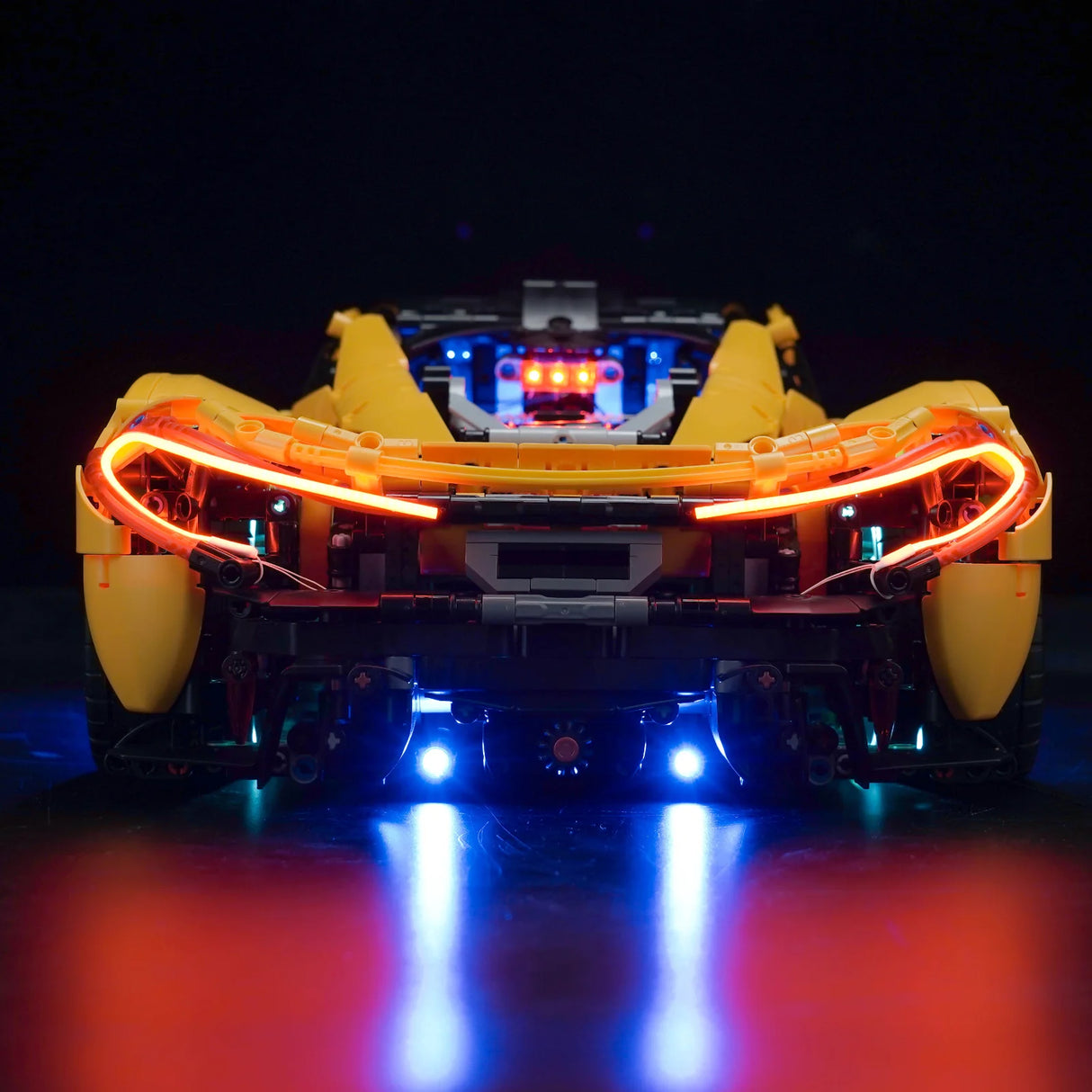 Gelbes Lego Technic Modellauto von hinten mit leuchtenden orangefarbenen Rücklichtern und blauer Unterbodenbeleuchtung