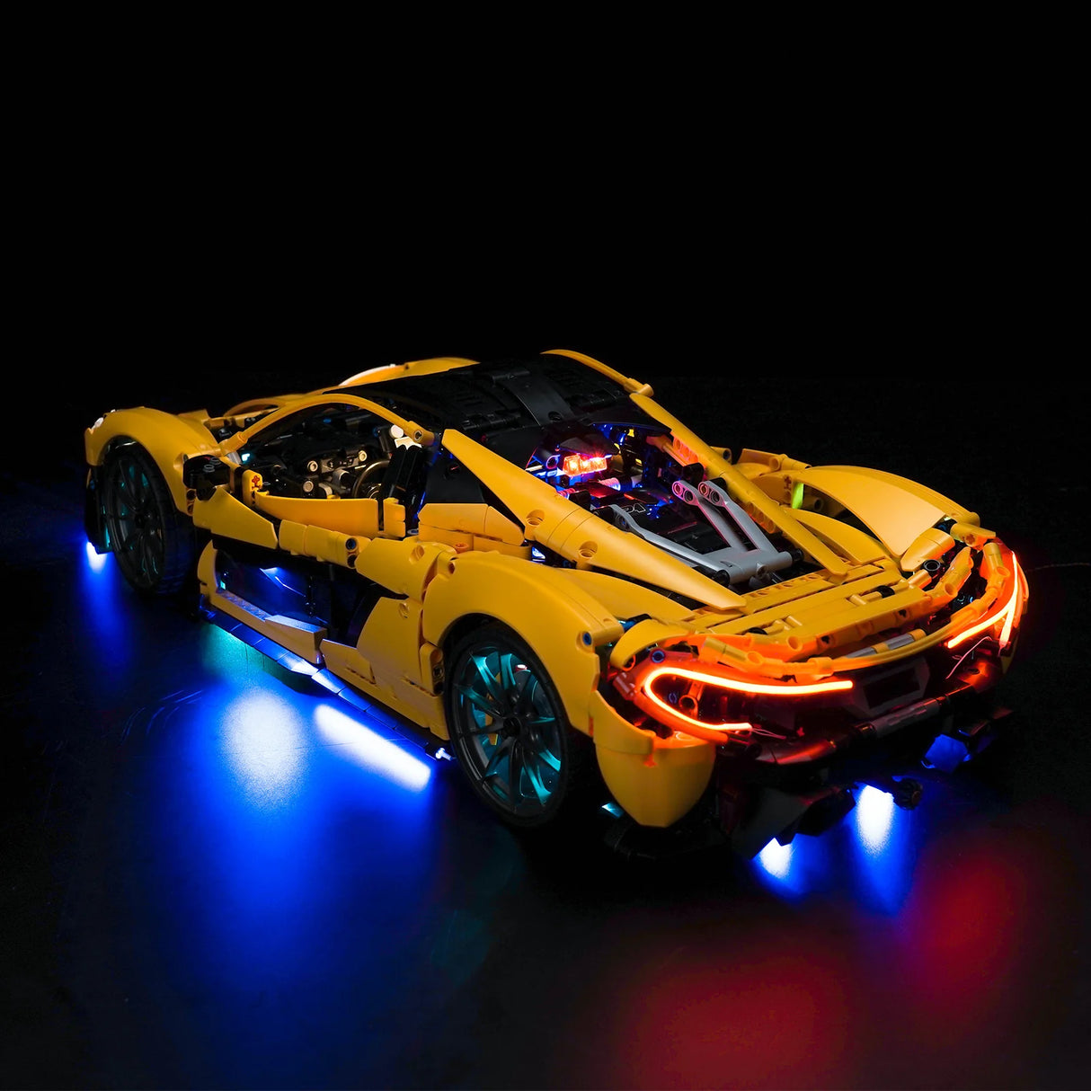 Gelbes Lego Technic Modellauto mit blauer Unterbodenbeleuchtung und leuchtenden Rücklichtern auf schwarzem Grund