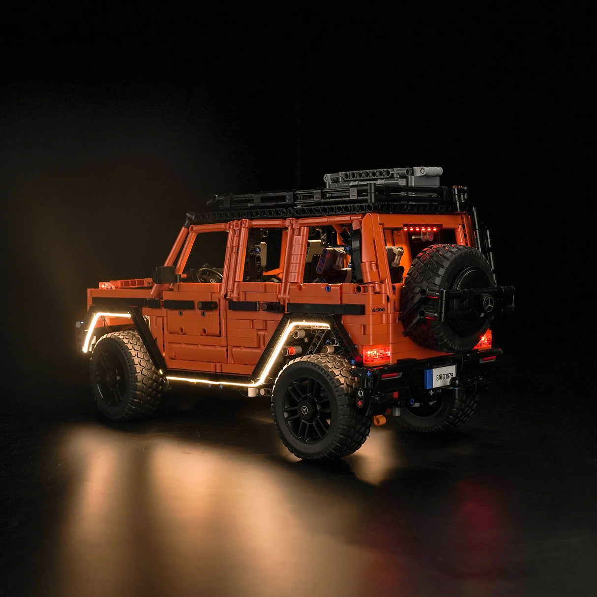 Orangefarbenes Mercedes G-Klasse Modell aus Klemmbausteinen mit eingeschalteter Beleuchtung vor schwarzem Hintergrund