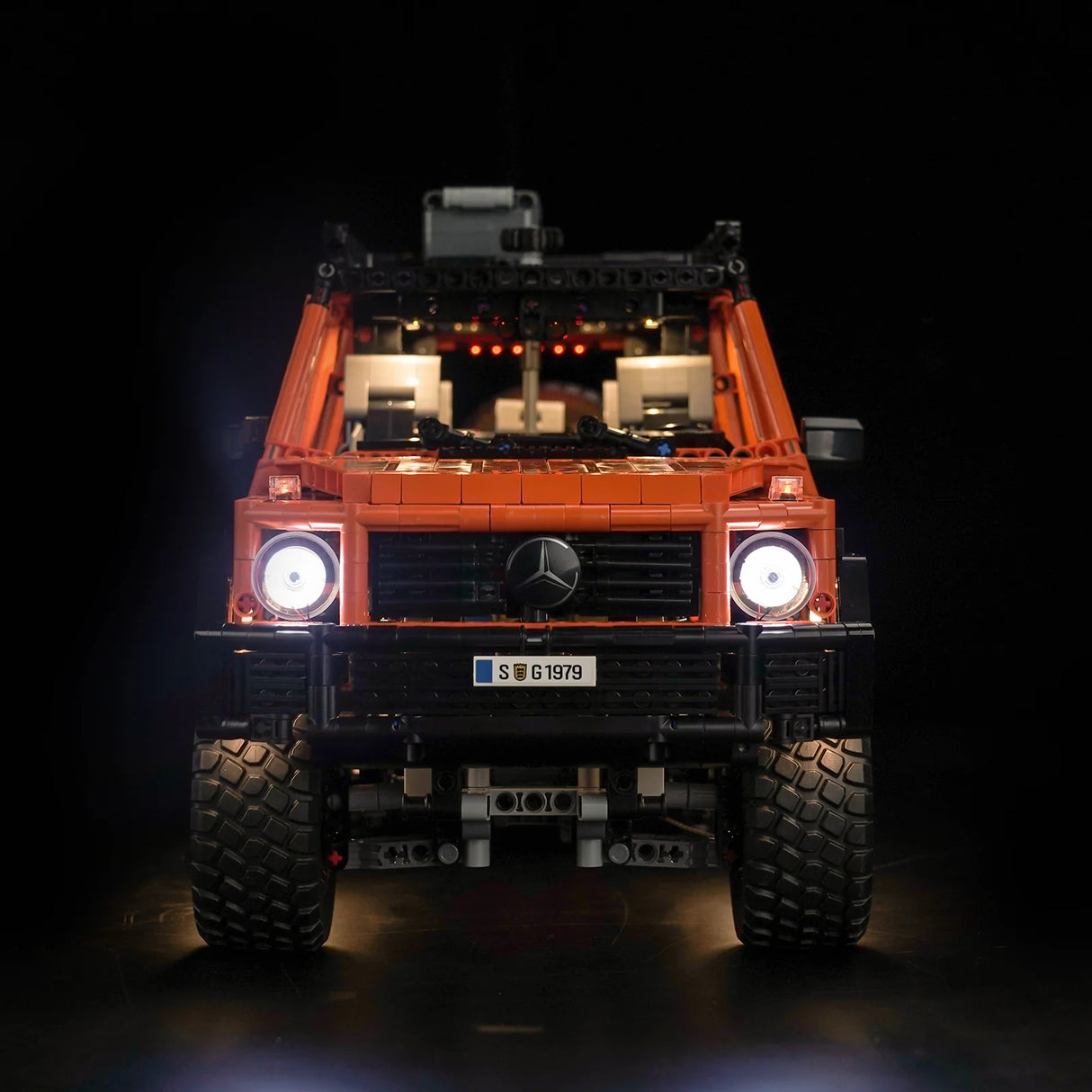 Orangefarbenes Mercedes G-Klasse Modell aus Bausteinen mit eingeschalteten Frontscheinwerfern vor schwarzem Hintergrund
