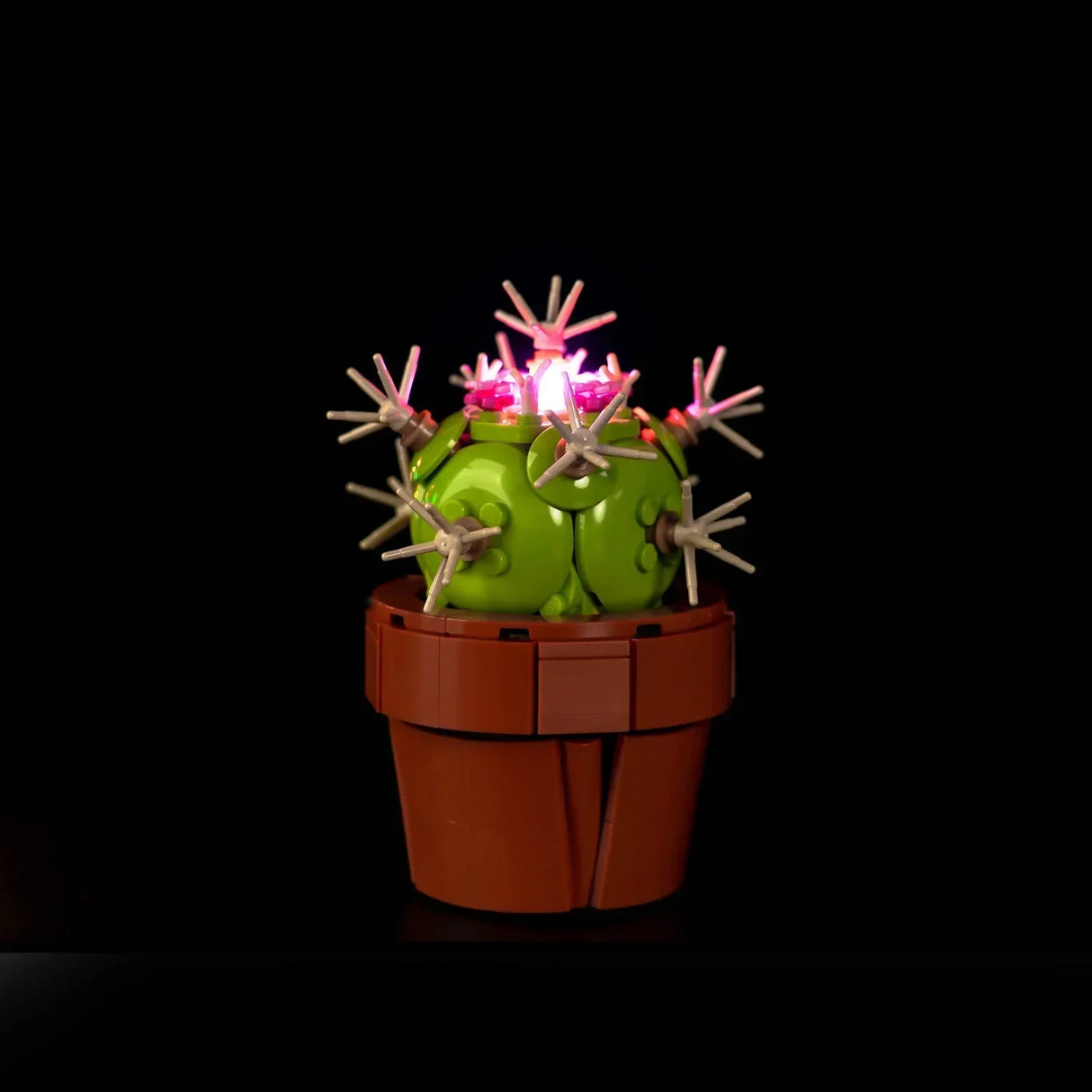 Ein runder LEGO Kaktus mit weißen Stacheln aus dem Set Mini-Pflanzen (10329), der an der Spitze mit einem rosafarbenen LED-Licht stimmungsvoll beleuchtet wird.