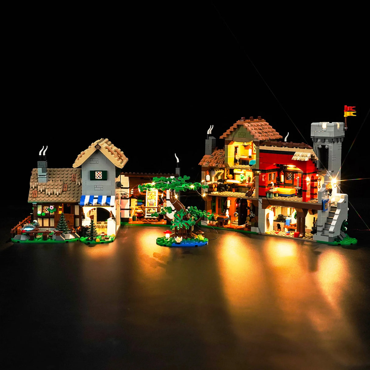 Beleuchtetes Lego Mittelalterdorf mit Fachwerkhäusern und Baum vor schwarzem Hintergrund