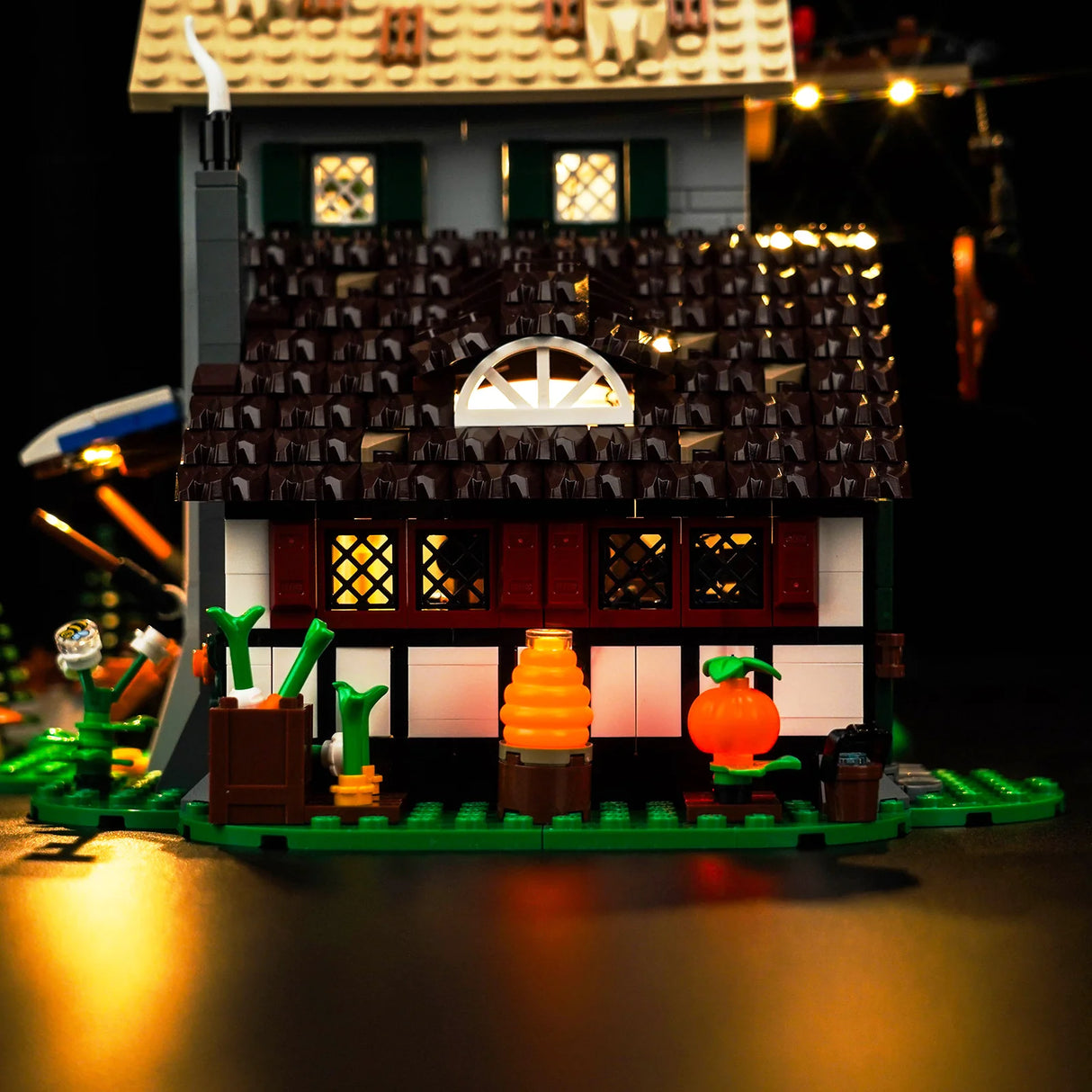 Beleuchtetes Lego Haus mit Garten und Kürbis vor dunklem Hintergrund