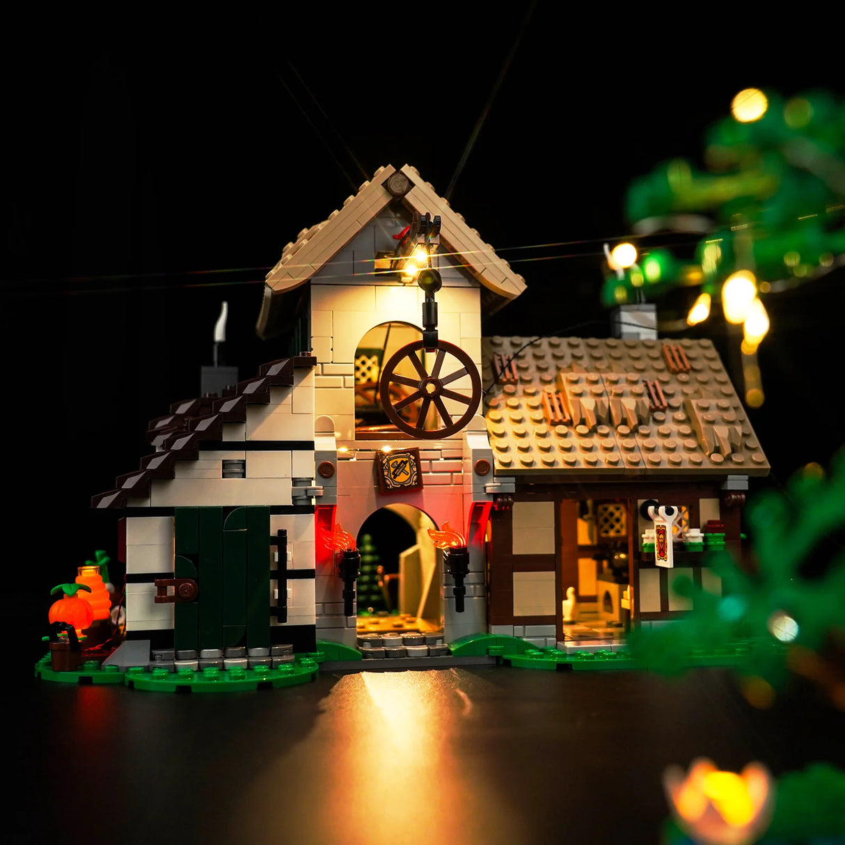 Beleuchtetes Lego Mittelalterhaus mit Rad und Fackeln vor schwarzem Hintergrund