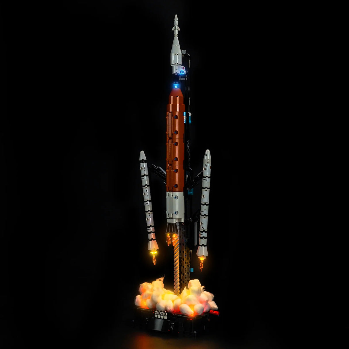 Ein Lego-Modell einer Rakete mit orangefarbenem Rumpf und weißen Boostern, die mit Lichtern und Rauch startet
