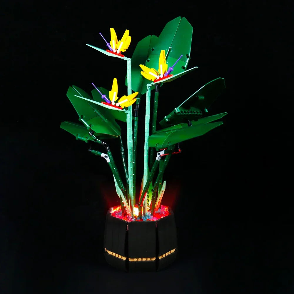 Beleuchtete Paradiesvogelblume aus Klemmbausteinen in einem schwarzen Topf vor schwarzem Hintergrund