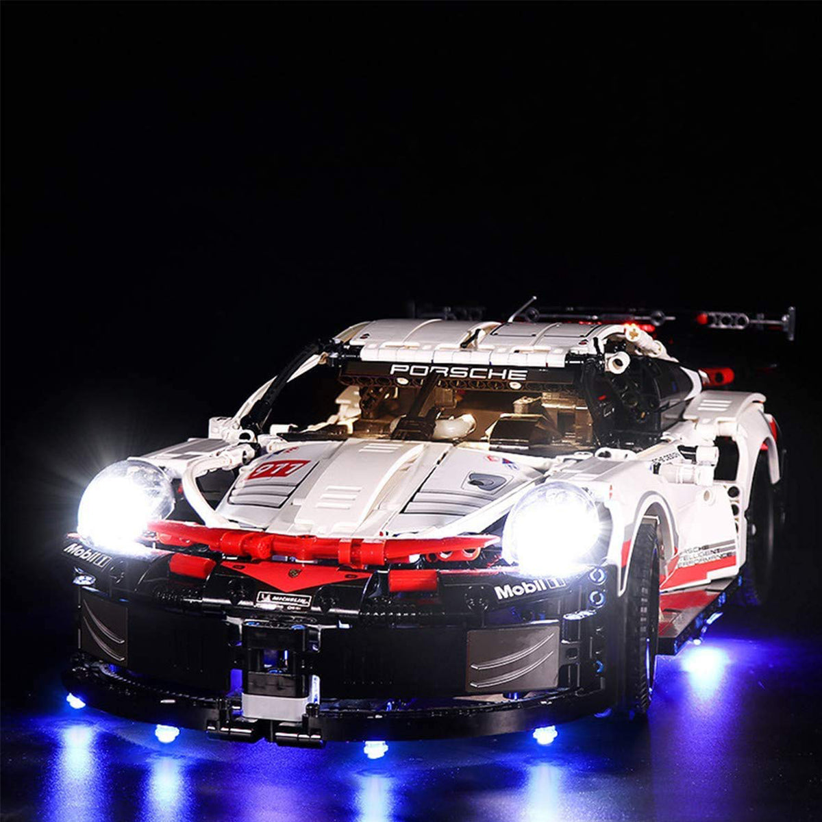 Weißes Lego Technic Porsche Modell mit eingeschalteter LED Beleuchtung vor schwarzem Hintergrund