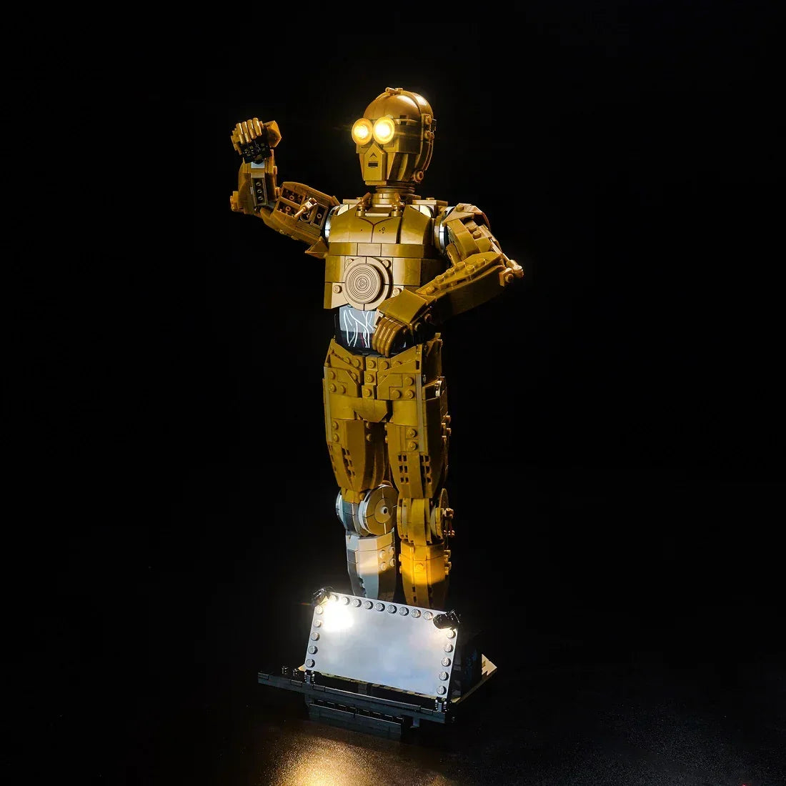 Lego C-3PO Figur mit leuchtenden Augen auf einem beleuchteten Sockel vor schwarzem Hintergrund