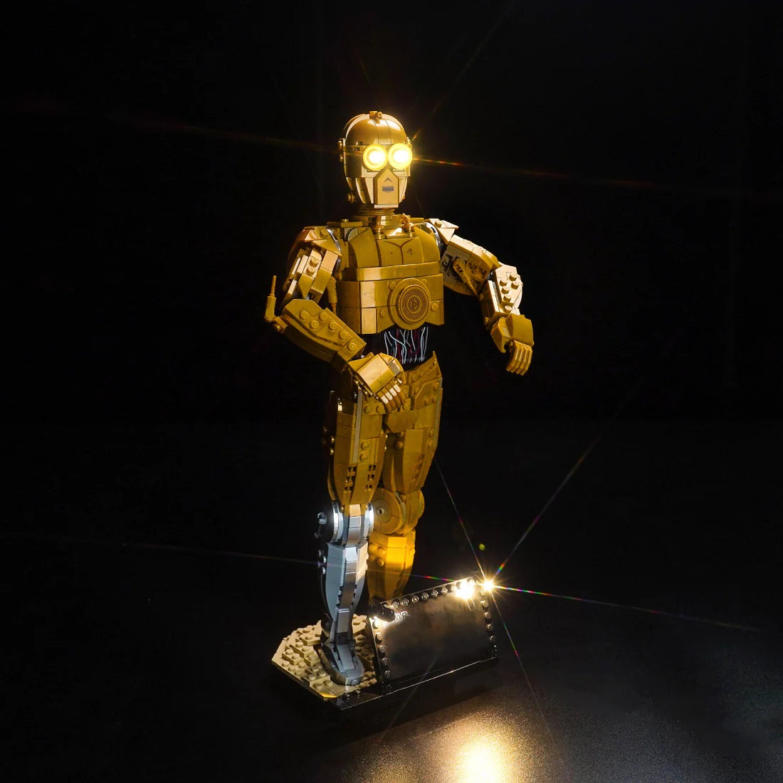 Lego C-3PO Figur mit leuchtenden Augen auf einem schwarzen Sockel vor dunklem Hintergrund