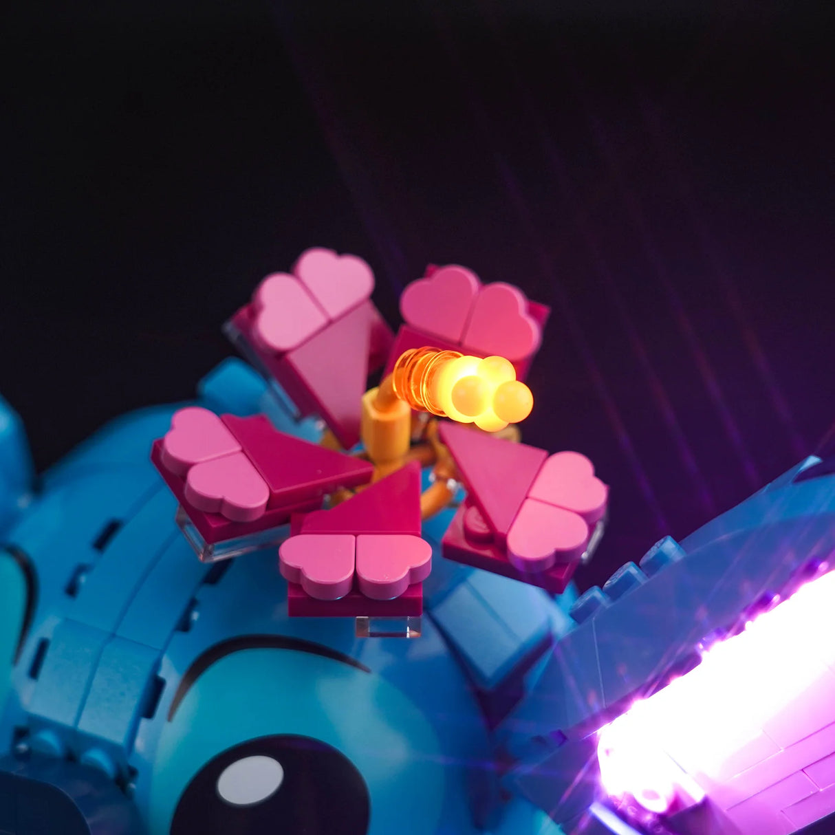 Lego Blume aus rosa und pinken Bausteinen auf einer blauen Figur mit leuchtendem gelben Stempel