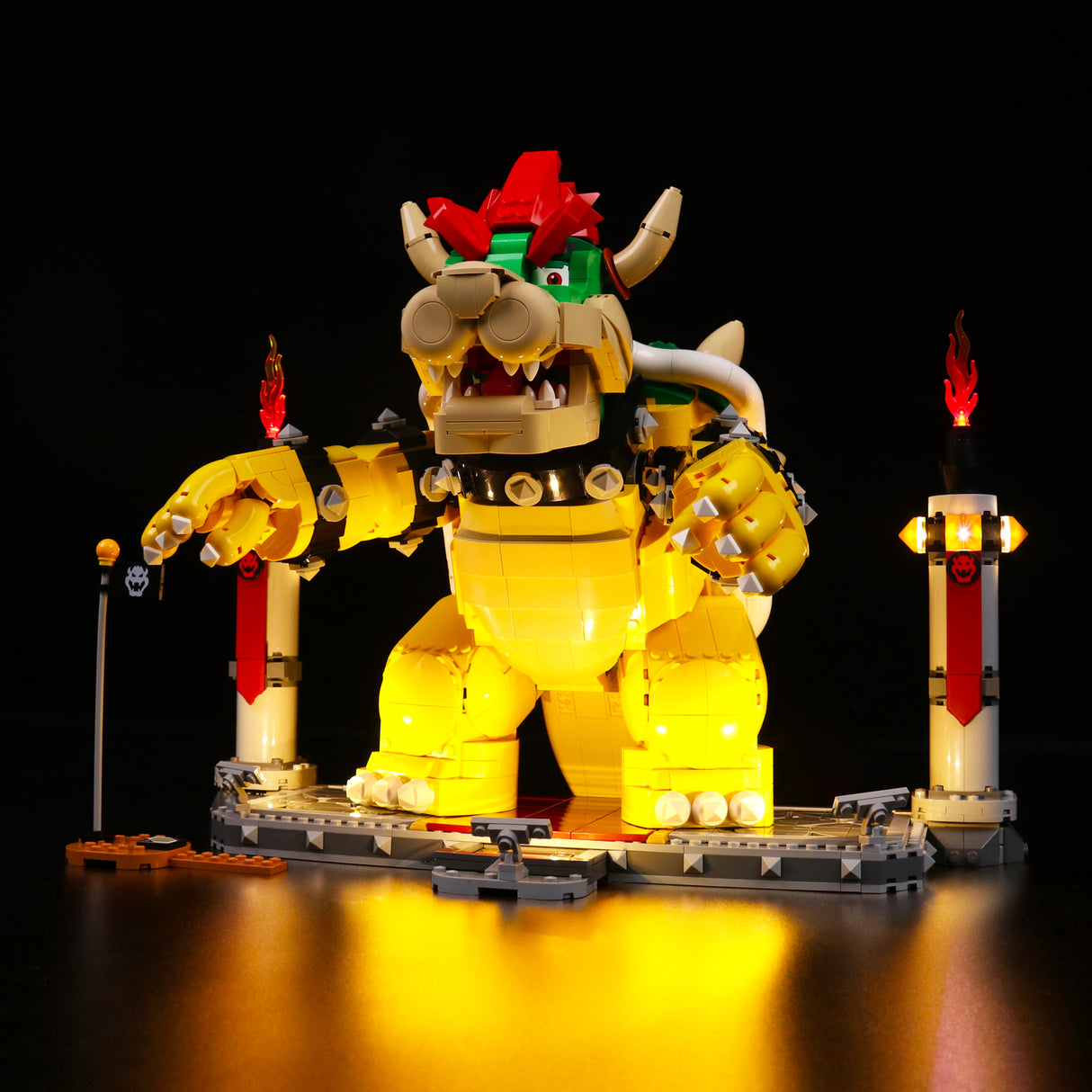 Beleuchtete Lego Bowser Figur auf einer Plattform mit zwei Fackeln vor schwarzem Hintergrund
