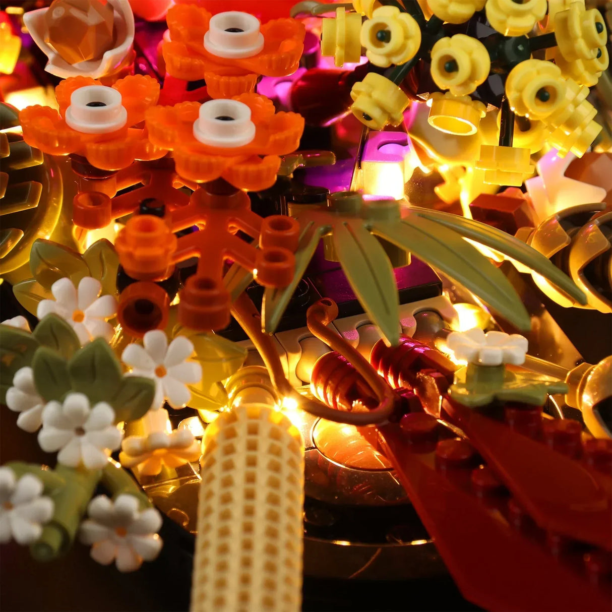 Detailansicht der LED-Lichterkette, die dezent unter den herbstlichen Blättern und kleinen weißen Blüten des LEGO Botanical Trockenblumengestecks verlegt ist.