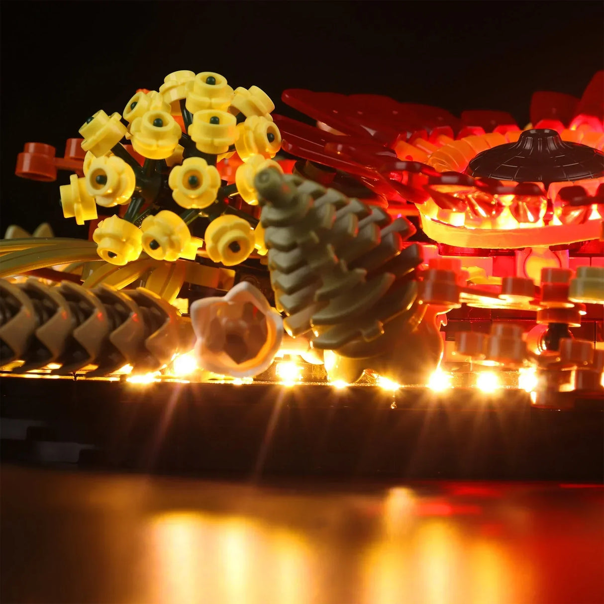 Seitenansicht des beleuchteten LEGO Trockenblumengestecks bei Nacht mit warmweißen LED-Lichtern unter den Tannenzapfen und gelben Blüten.