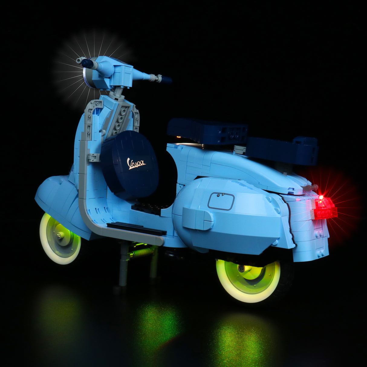 Hellblaues Vespa Modell aus Klemmbausteinen mit leuchtenden Scheinwerfern und Rücklicht vor schwarzem Hintergrund