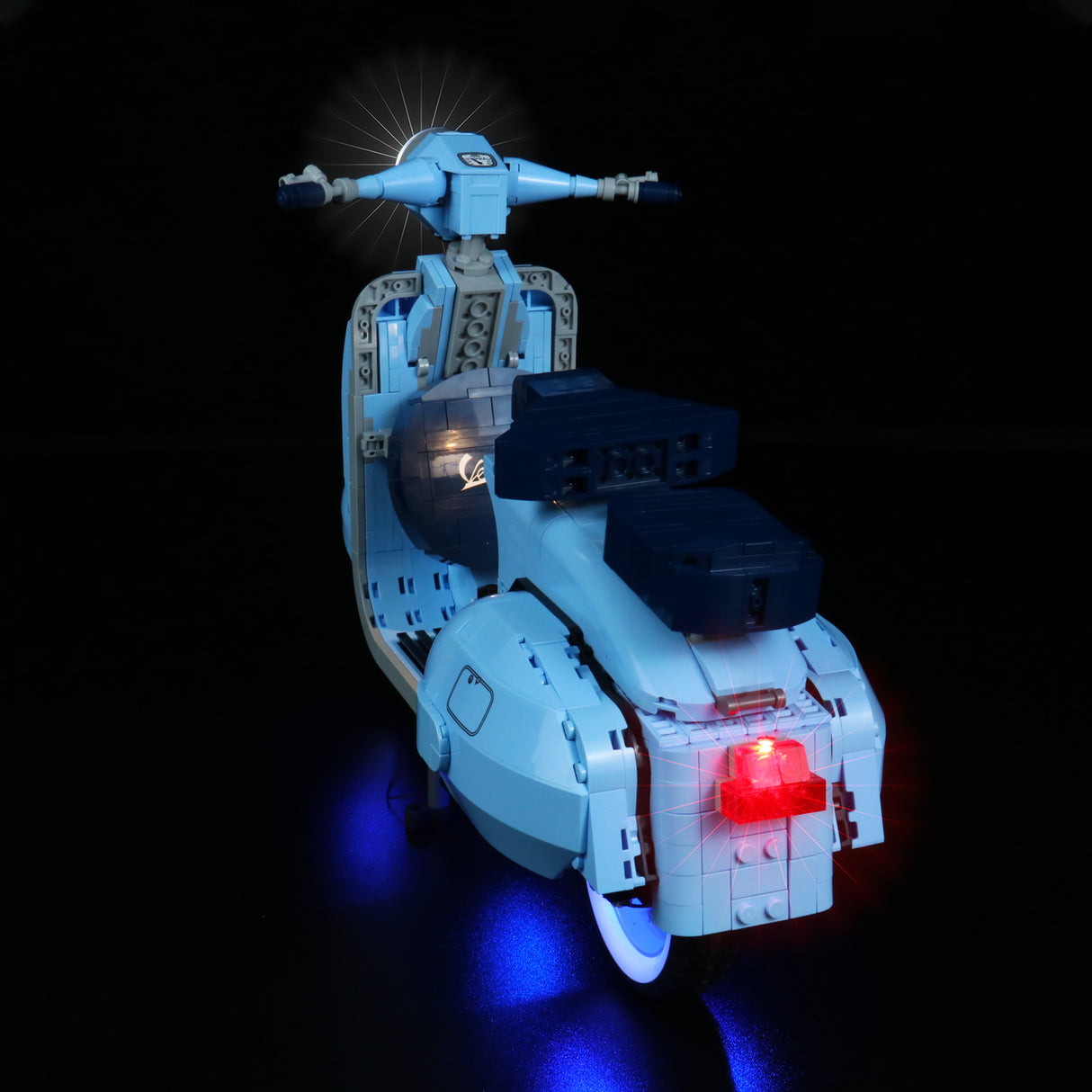 Hellblauer Lego Vespa Roller mit leuchtendem Frontscheinwerfer und rotem Rücklicht vor schwarzem Hintergrund