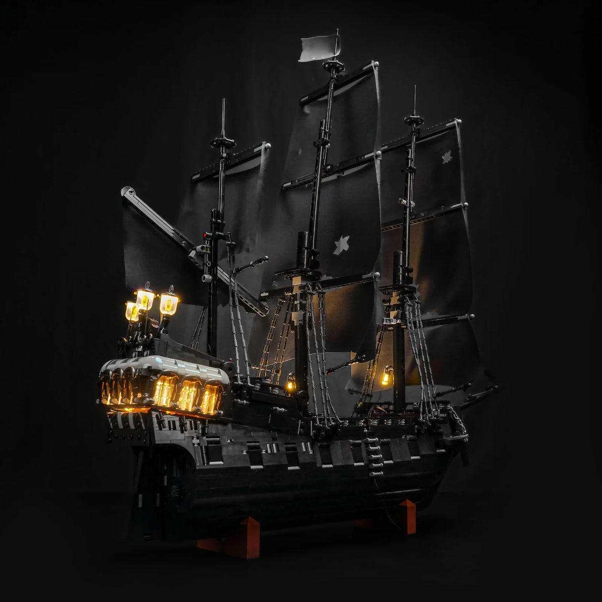 Beleuchtetes LEGO Piratenschiff mit schwarzen Segeln und goldenen Laternen auf schwarzem Hintergrund