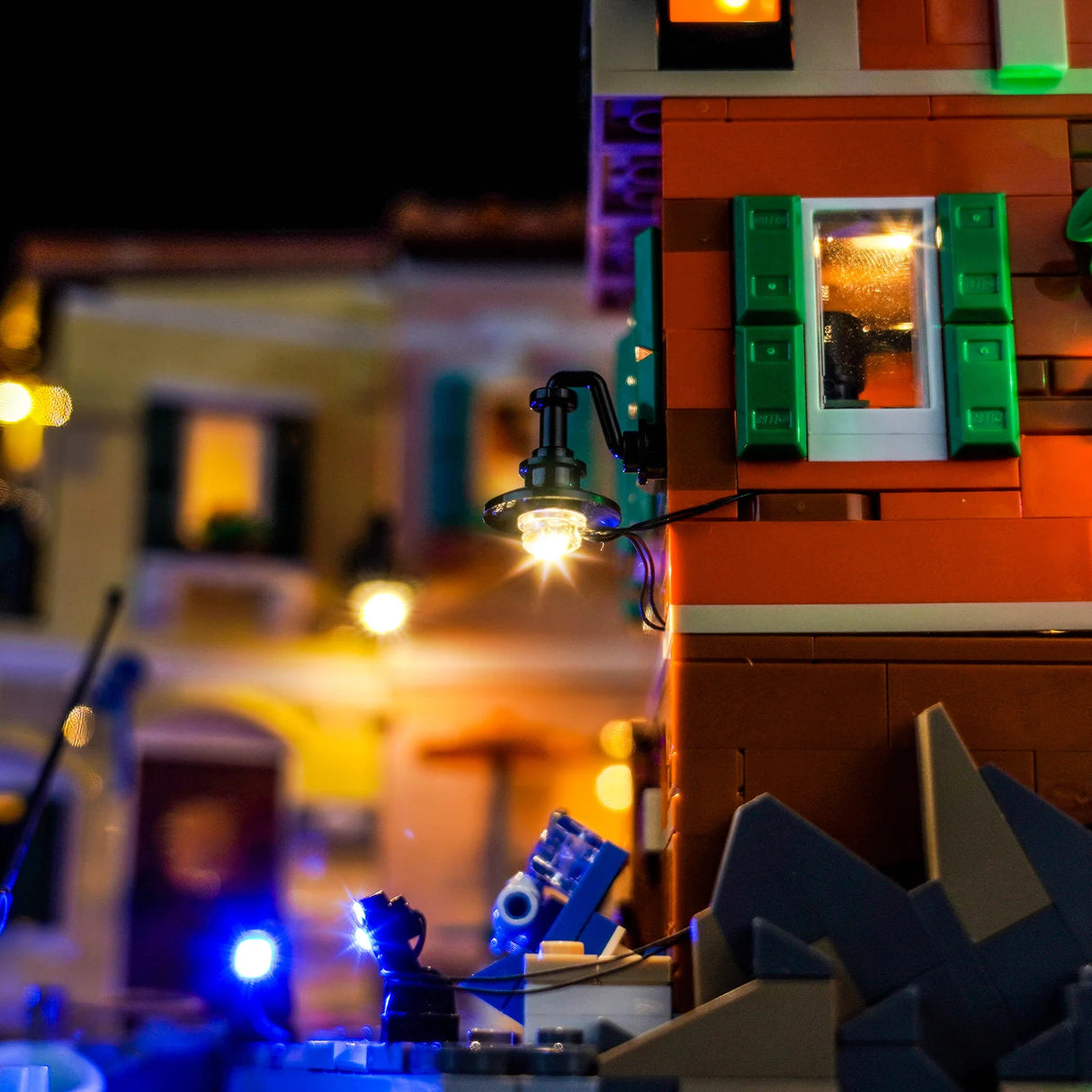 Nahaufnahme eines beleuchteten LEGO-Gebäudes mit Laterne und Fensterläden bei Nacht